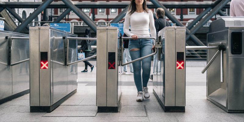 Dark-haired woman exiting through the magnetic turnstiles of access and exit in the subway station.