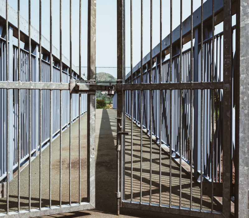 A metal gate padlocked closing off the bridge pathway to a scenic outdoor space