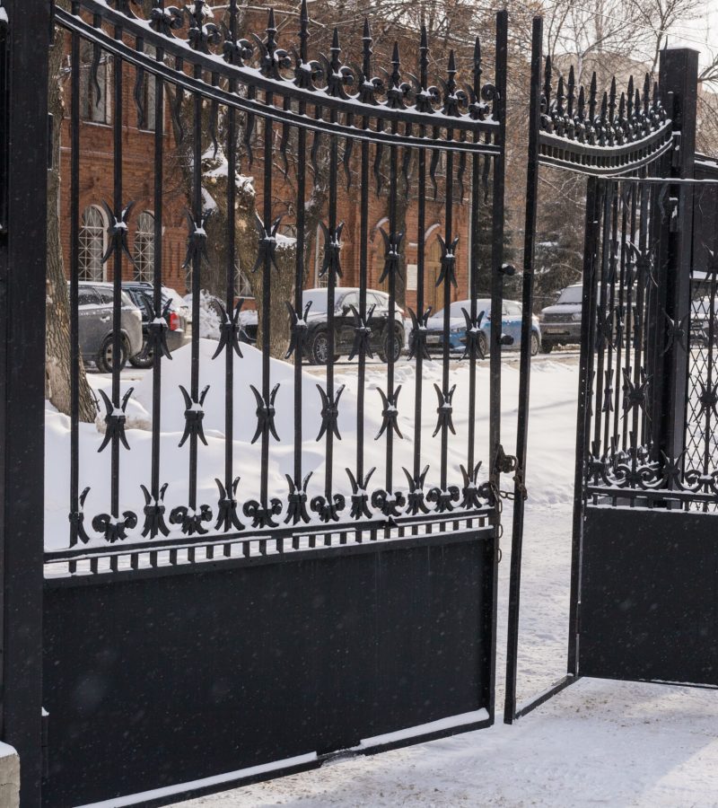 Old iron gate with ironwork unlocked with snowy scene falling and snow settling on metal. Winter city concept